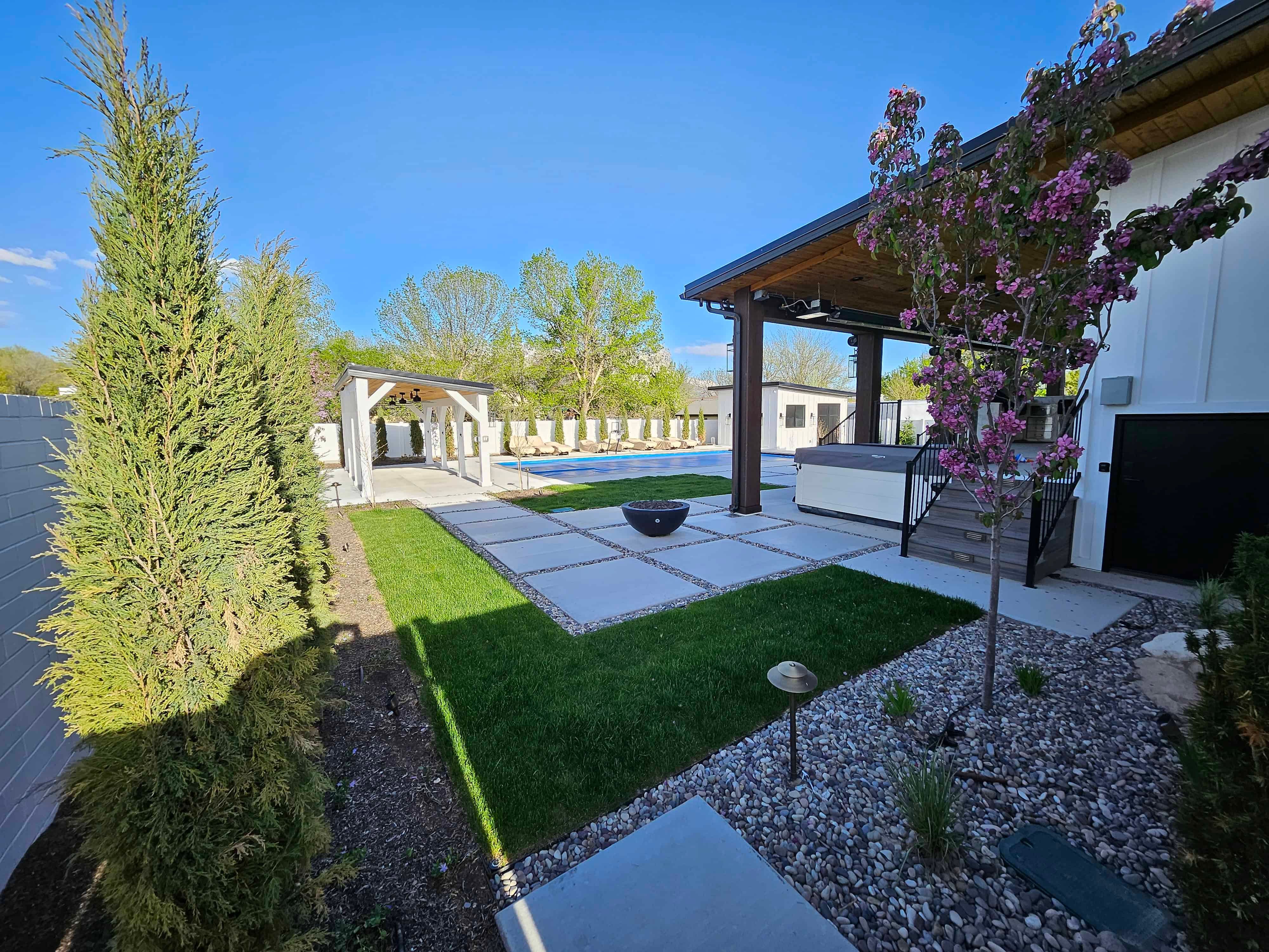 Modern landscape in South Jordan featuring a custom shade structure, concrete path, green lawn, and planted beds.