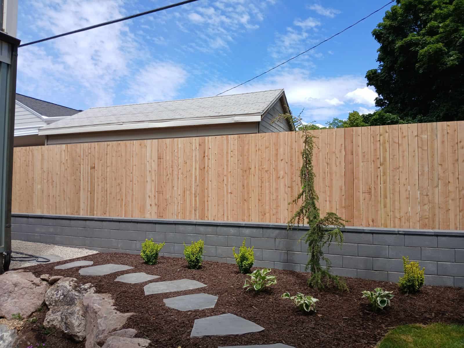 Millcreek backyard with a block retaining wall, cedar privacy fence, and natural flagstone walkway.