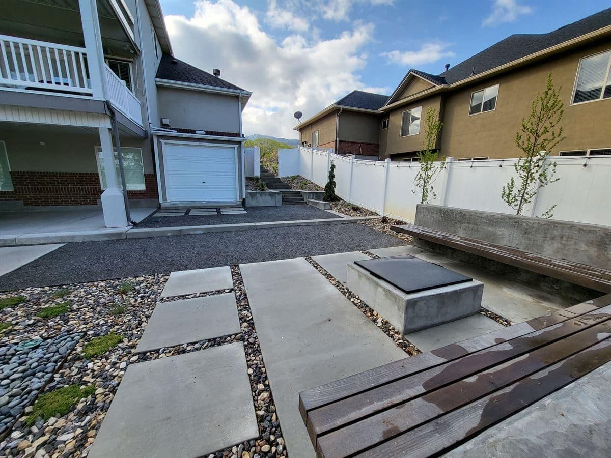 Bountiful backyard with modern concrete square pavers, fire pit patio, and built-in wood bench seating.