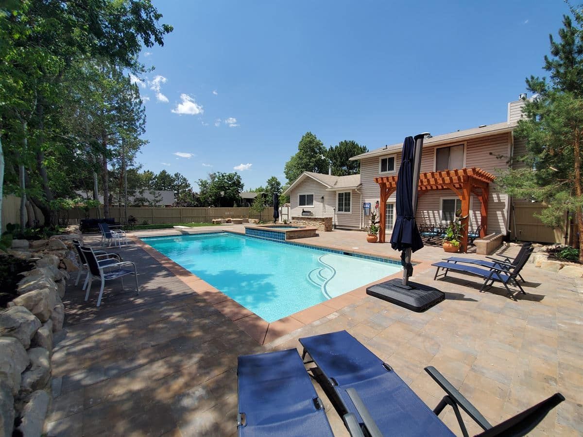 Pool view in Sandy from opposite side showing pergola, outdoor kitchen, and paver patio.