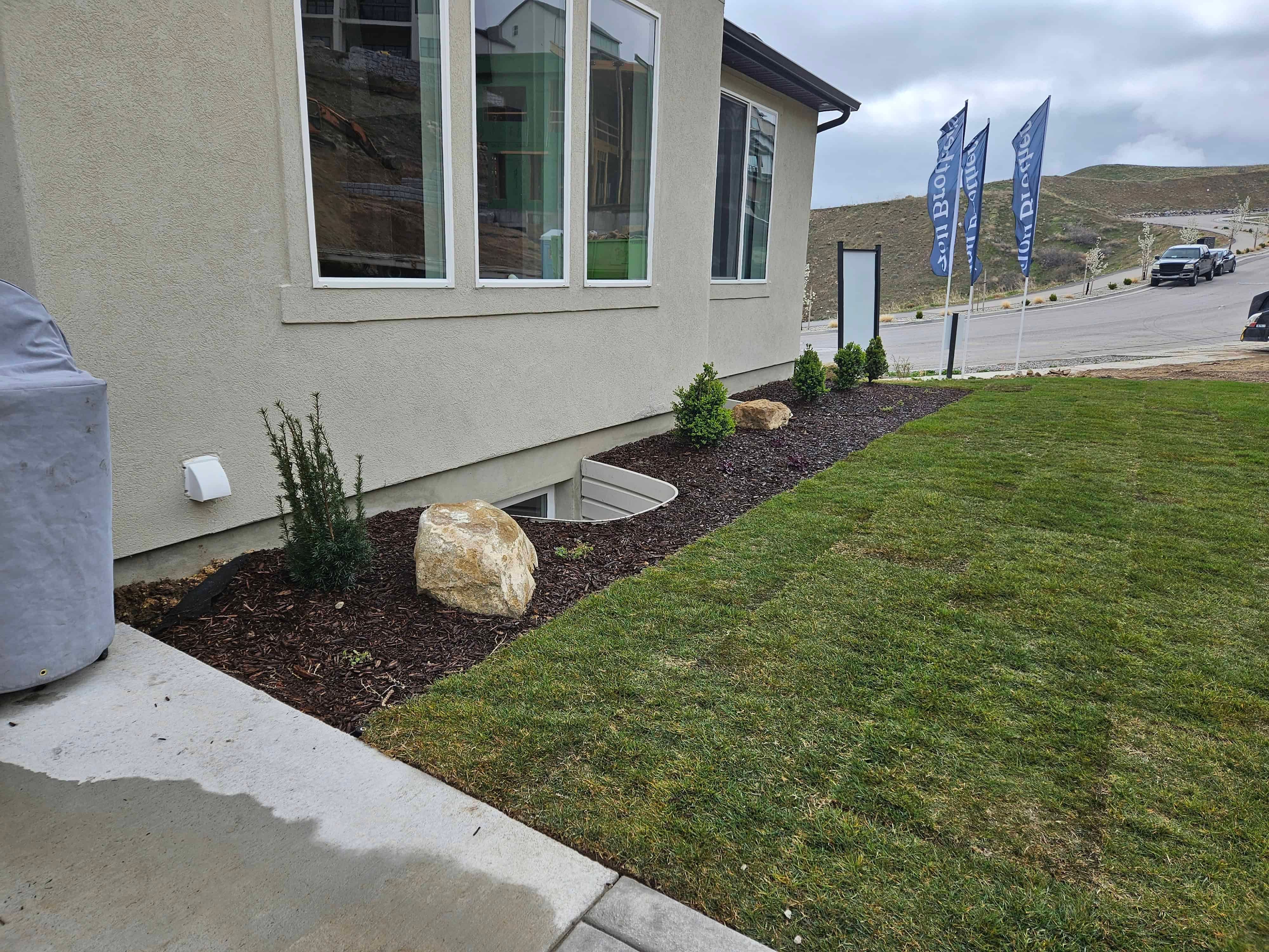 Finished backyard flower bed in Lehi, Utah with new plants and brown bark mulch.