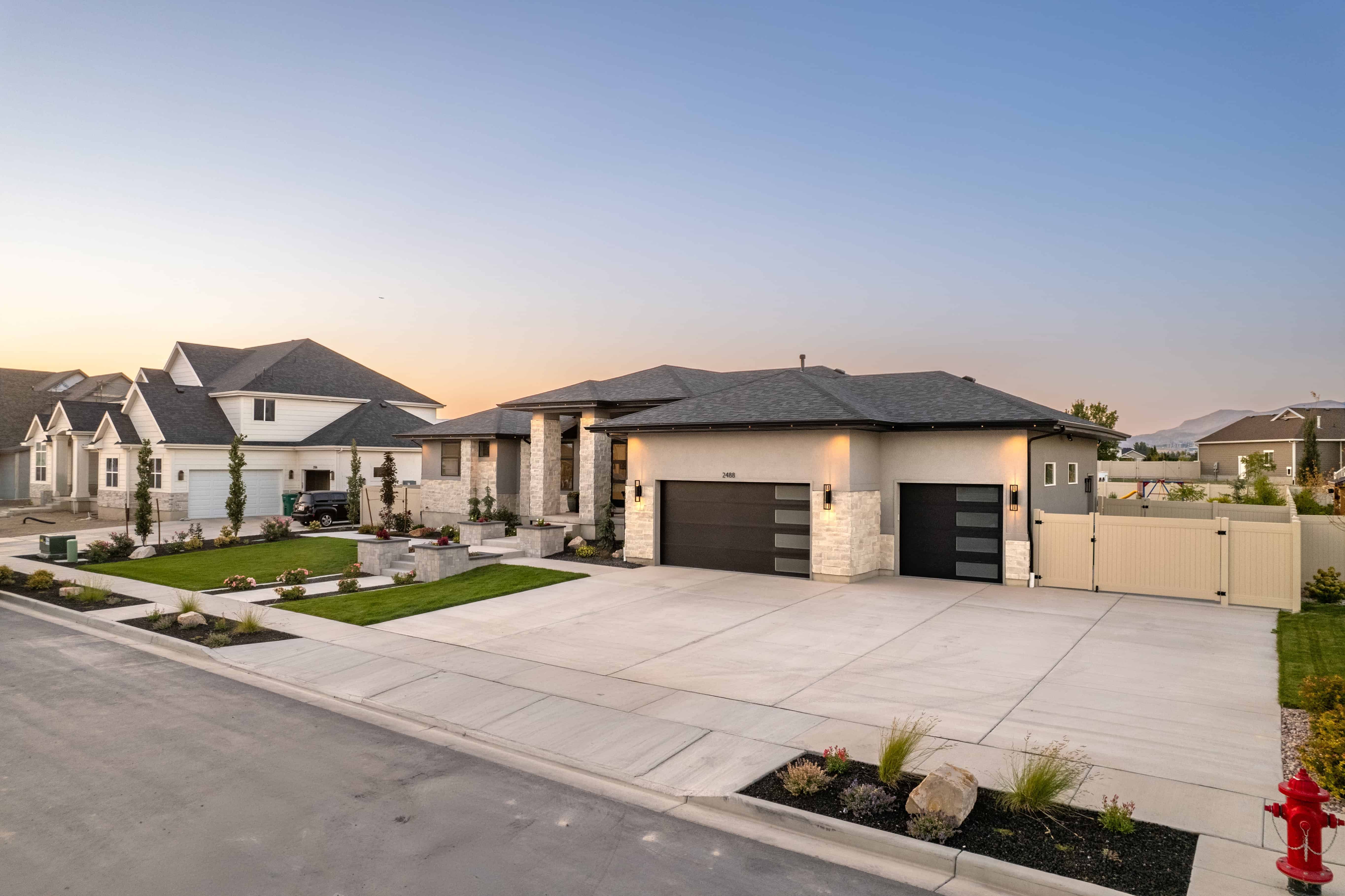 Completed concrete driveway and front walkway with landscaped planting beds at dusk.