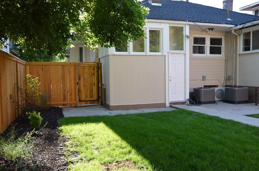 Backyard landscape with a wood gate, fresh planting bed, lawn, and concrete patio.