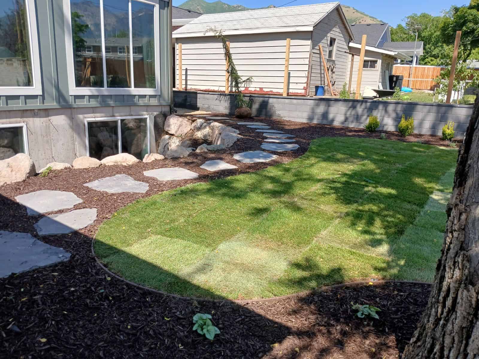 Backyard landscape with cedar fence, block retaining wall, flagstone path, and new lawn
