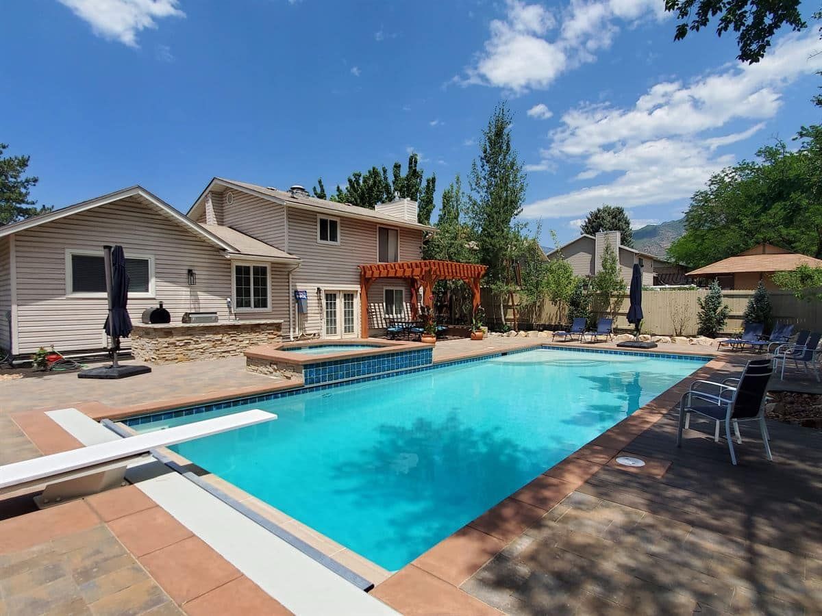 Swimming pool in Sandy looking toward pergola and custom outdoor kitchen with paver deck.