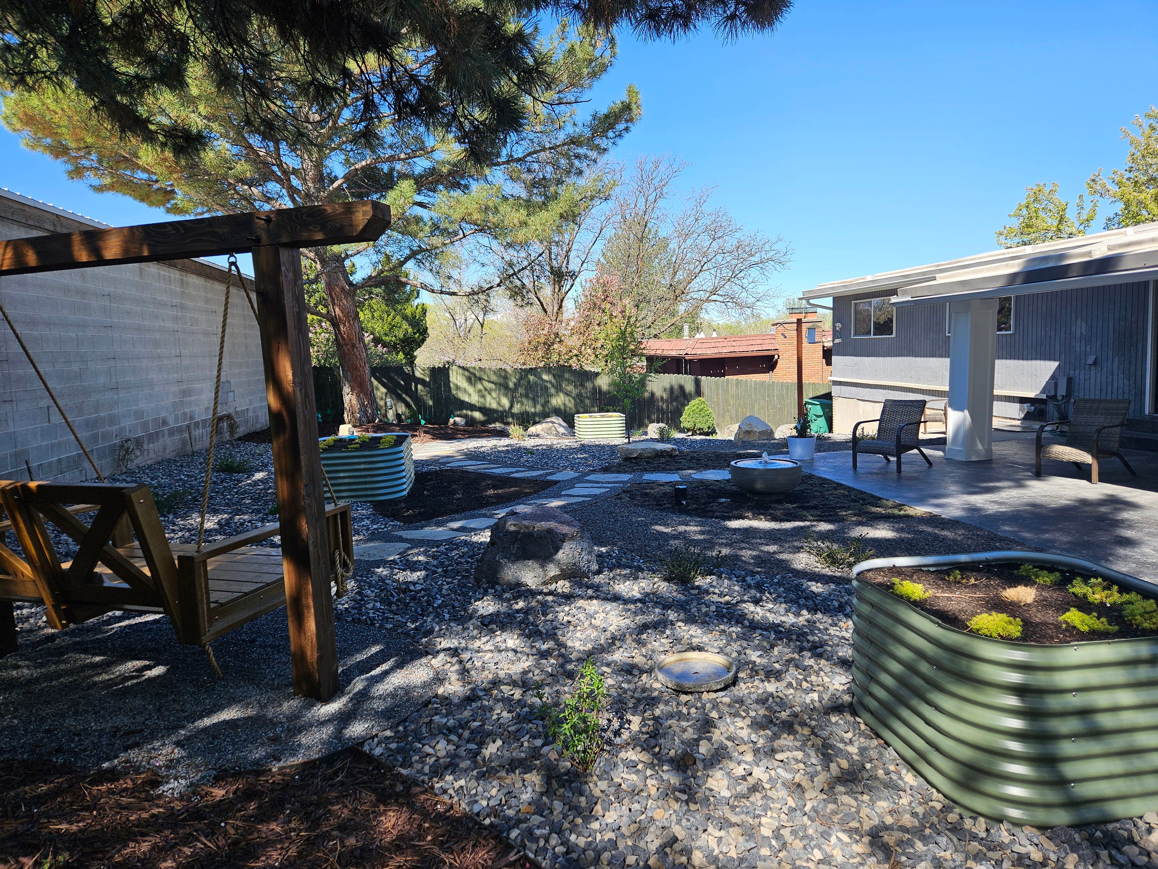 Complete landscape design in Murray, Utah featuring xeriscape elements, raised garden boxes, a water fountain, swing structure, and vibrant plants.