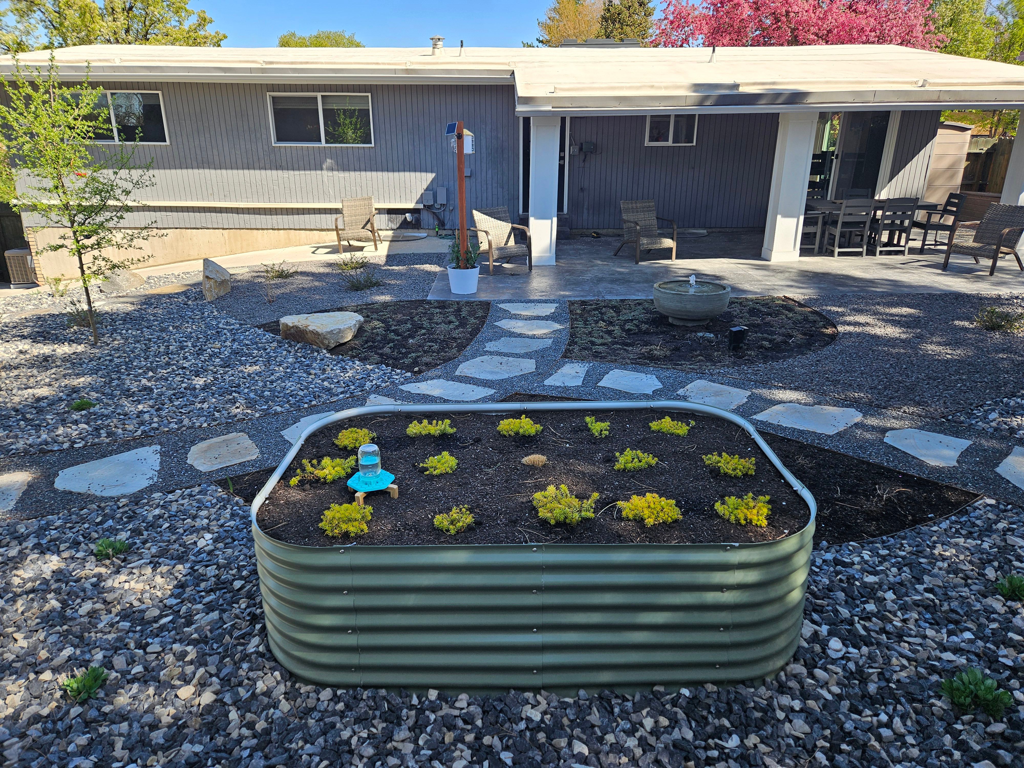 Raised garden bed integrated into a xeriscape landscape design in Murray with gravel and drought-tolerant plants.