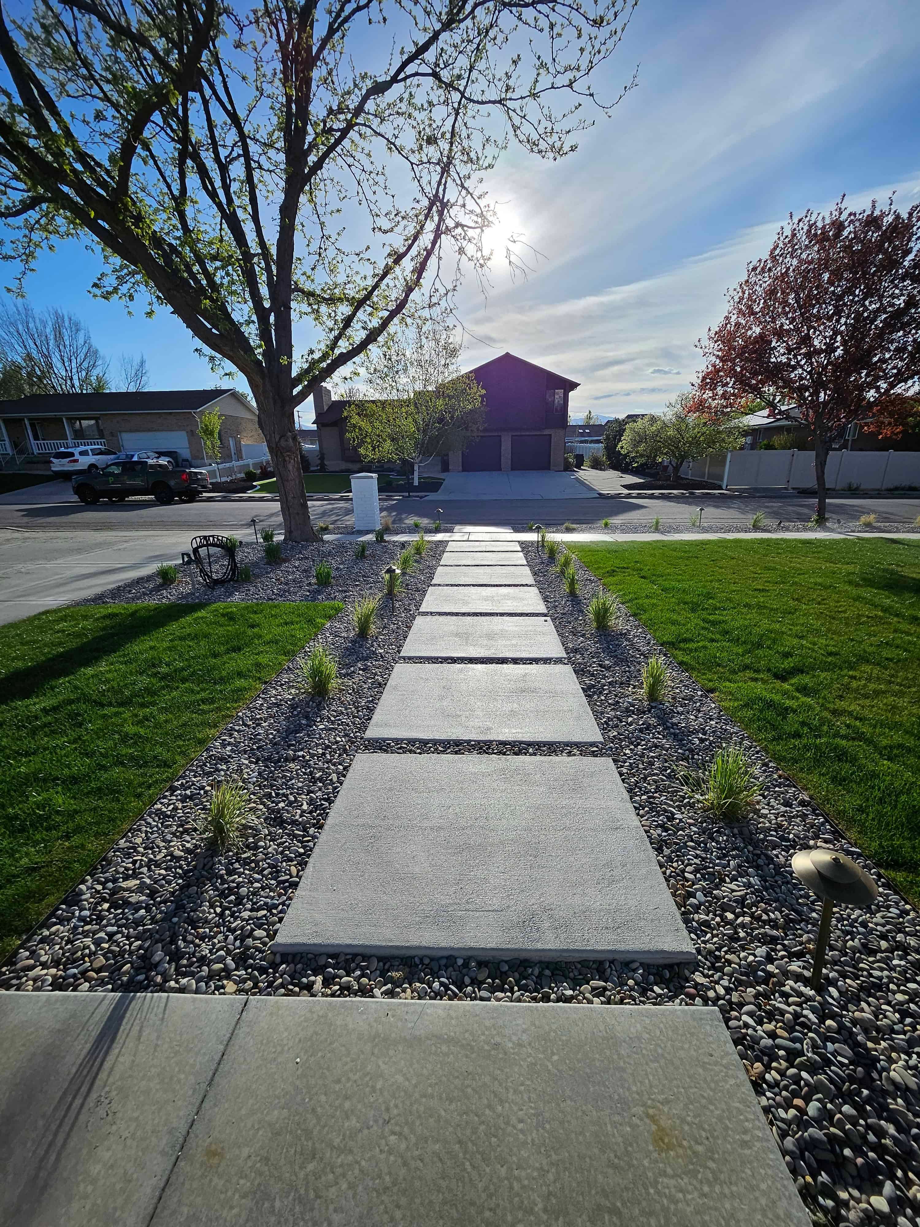 Front yard in South Jordan with a modern concrete walkway bordered by ornamental grasses and decorative gravel.