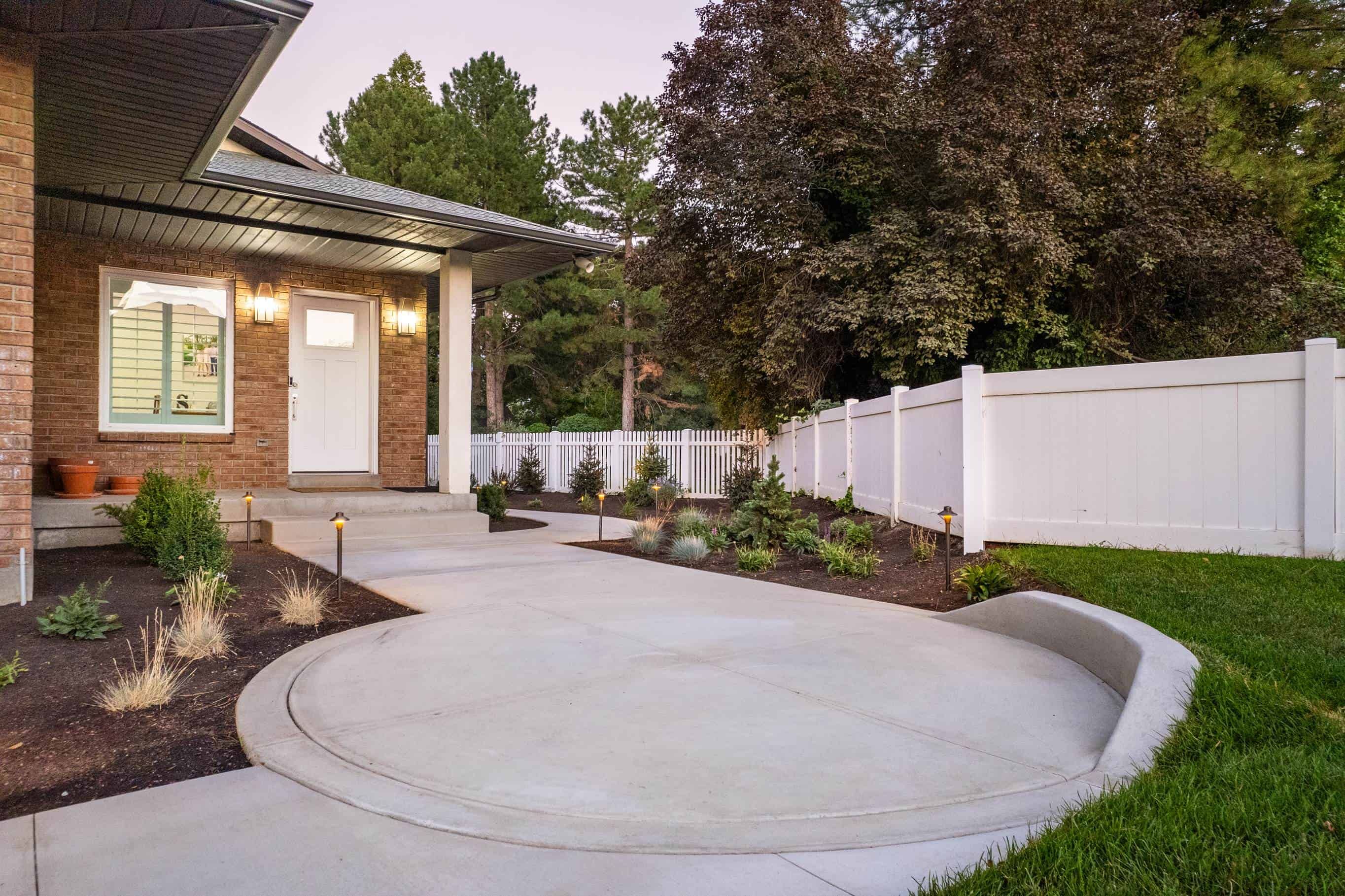 Curved concrete entry pad with low-voltage path lights, new planting beds, and white privacy fencing.