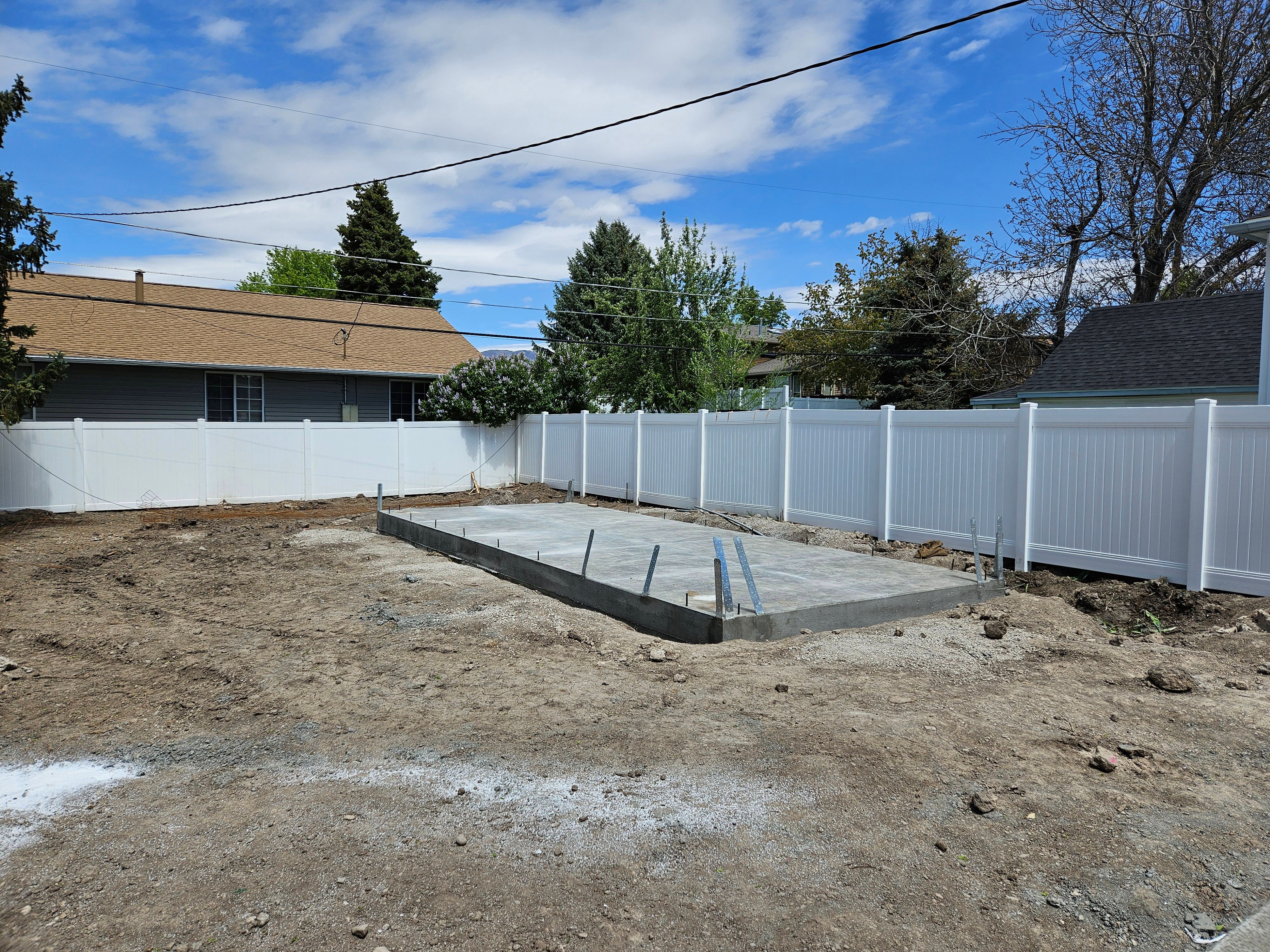 Concrete foundation slab preparation for a detached garage in a fenced backyard.