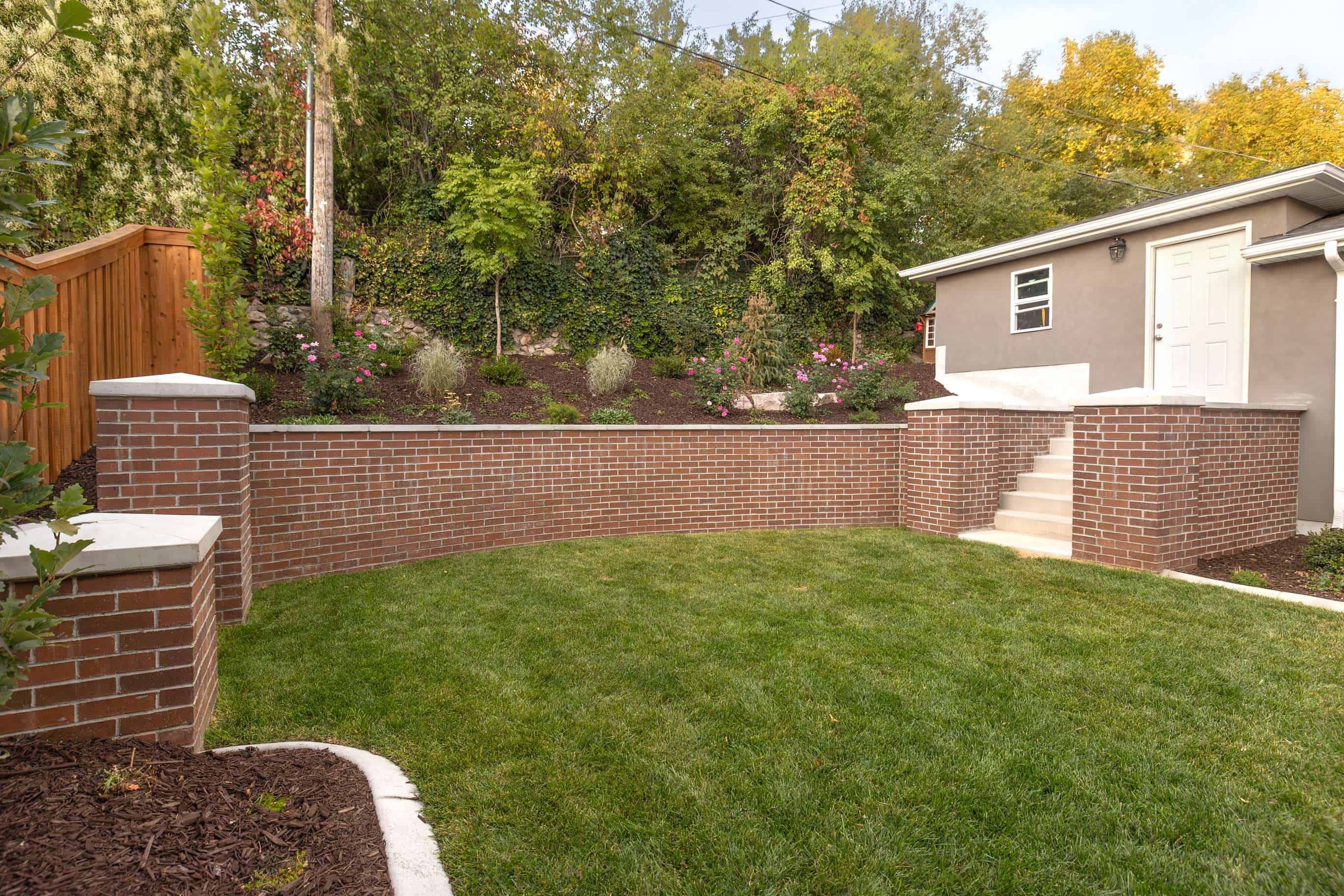 Custom red brick retaining wall with pillars and gray concrete caps installed in Federal Heights, Utah.