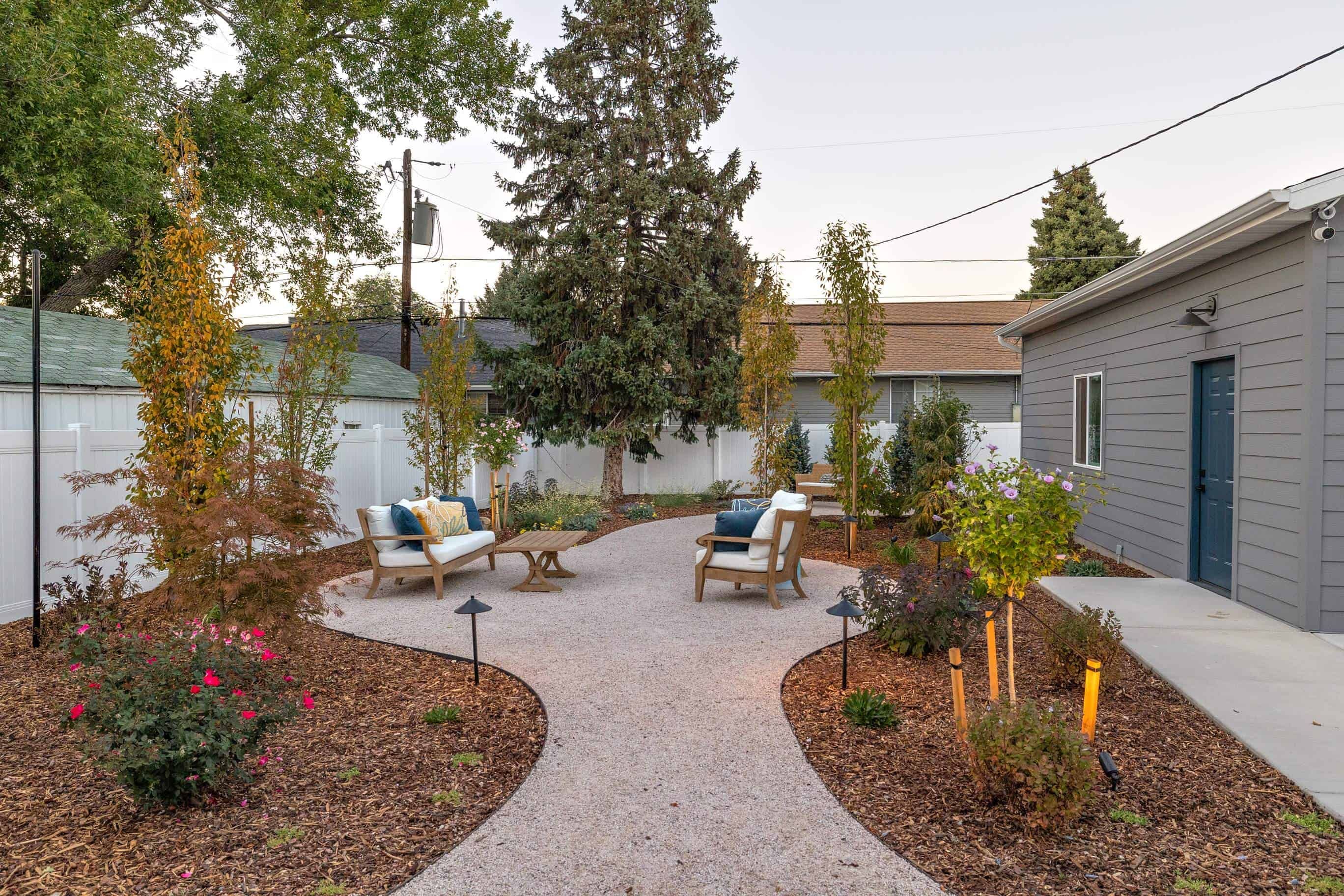 Curving gravel garden path with lounge seating, layered planting, and landscape lighting