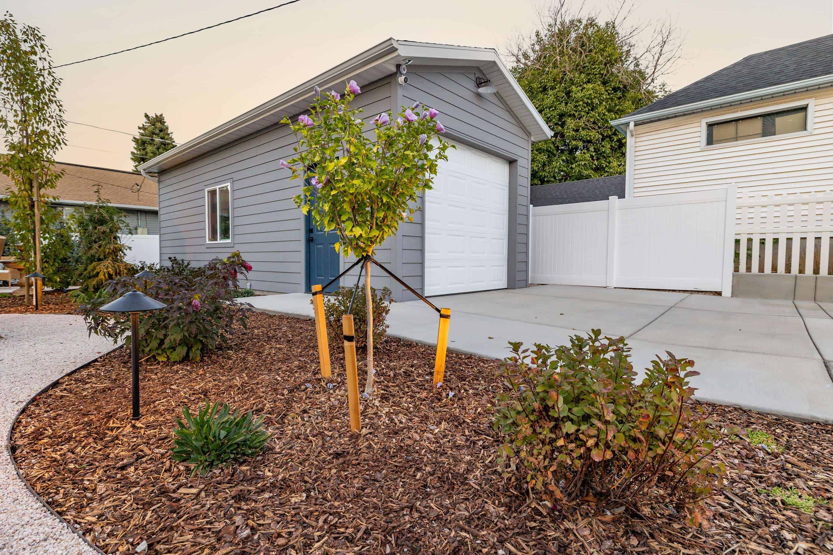 Finished detached garage framed by water-wise planting beds, mulch, and path lighting.