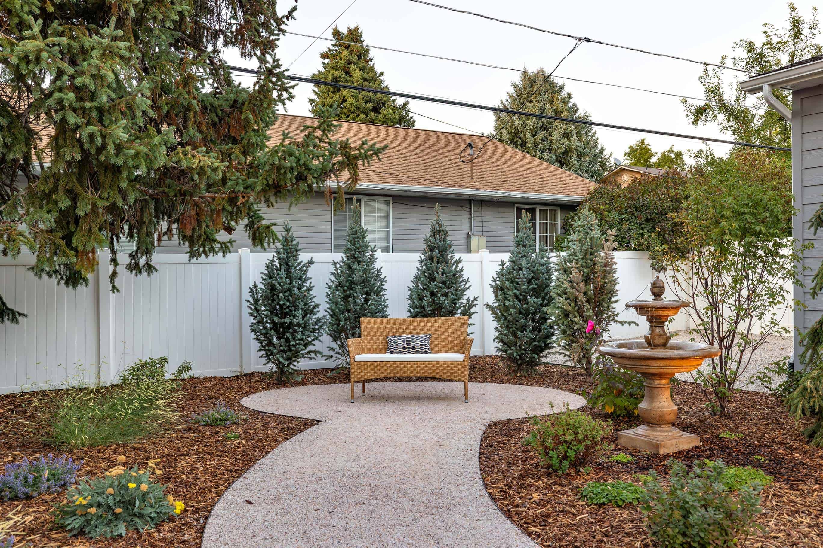 Curved gravel garden path with a bench, fountain, mulch beds, and drought-tolerant plantings