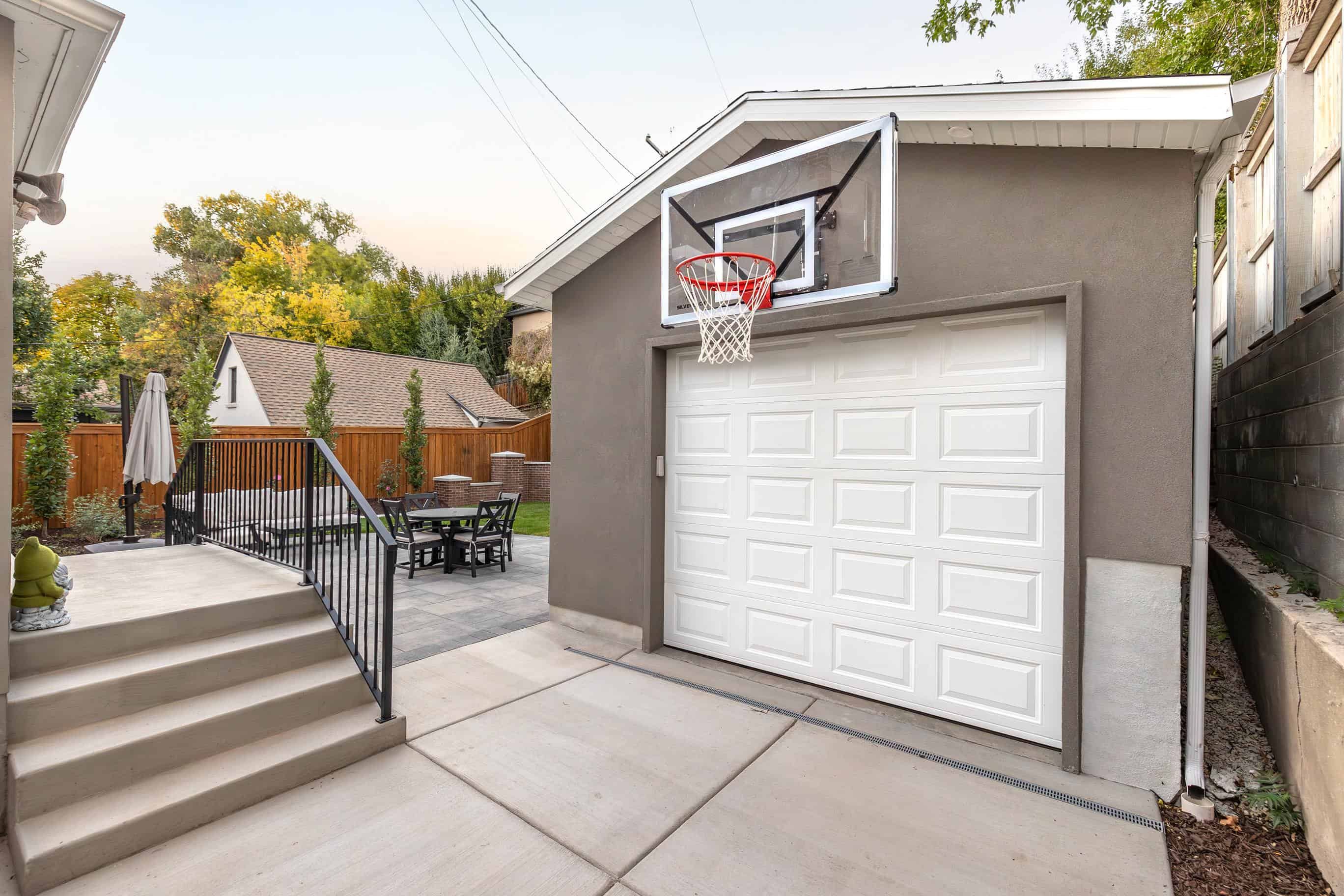 Front view of a completed detached garage with concrete drive, basketball hoop, and adjacent paver patio.