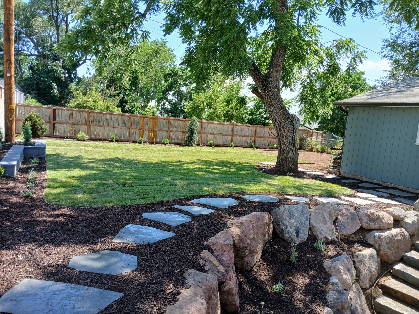 Backyard in Millcreek with a natural flagstone path, bark mulch, planting beds, and freshly laid sod.