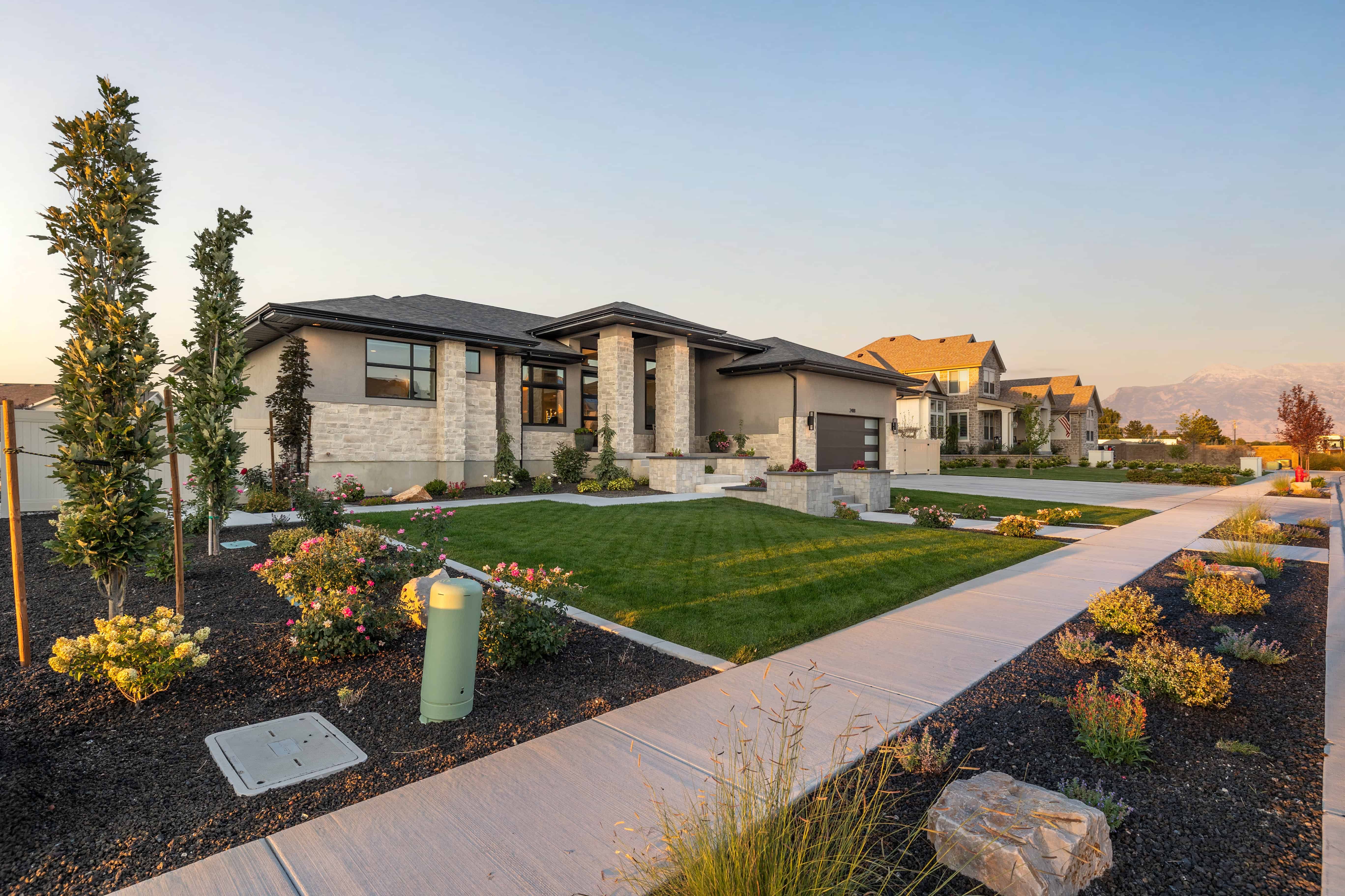 Finished front yard with concrete walkways, lawn, stone planters, and flowering beds