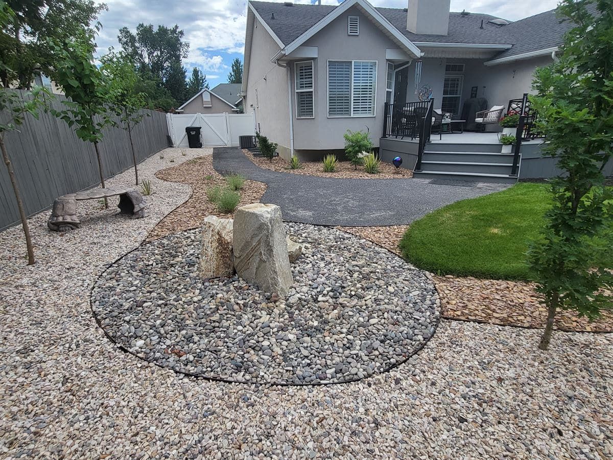 Completed low-water side-yard landscape with gravel, boulders, planting beds, and a curved path